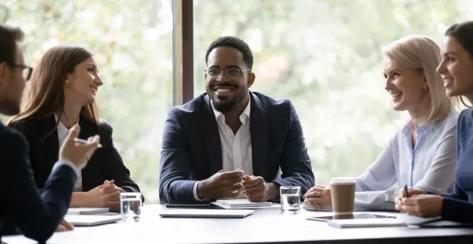 Smiling co-workers engaged in a conversation while sitting down at an office table