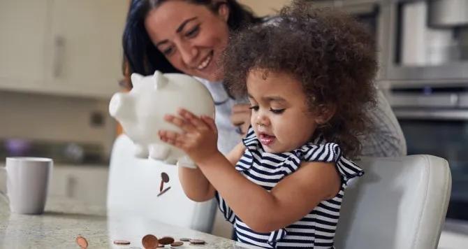 Proud mom with daughter holding a piggy bank shaking money out of it.