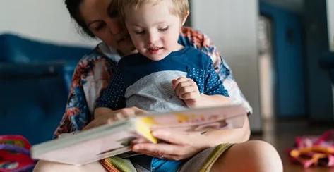 Woman holding special needs toddler on her lap and reading a book.