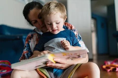Woman holding special needs toddler on her lap and reading a book.