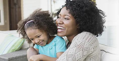 Mother with daughter on her lap as they smile and giggle together.