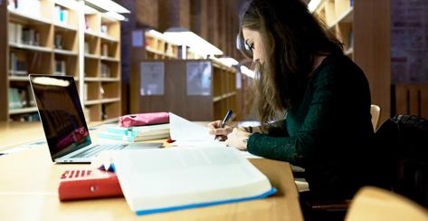 Side view of concentrated woman doing homework with laptop in library.