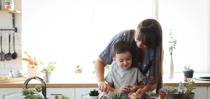 Ordinary mother and son transplant plants at the table in the kitchen in a real interior, the concept of education and creativity, care and environmental friendliness.