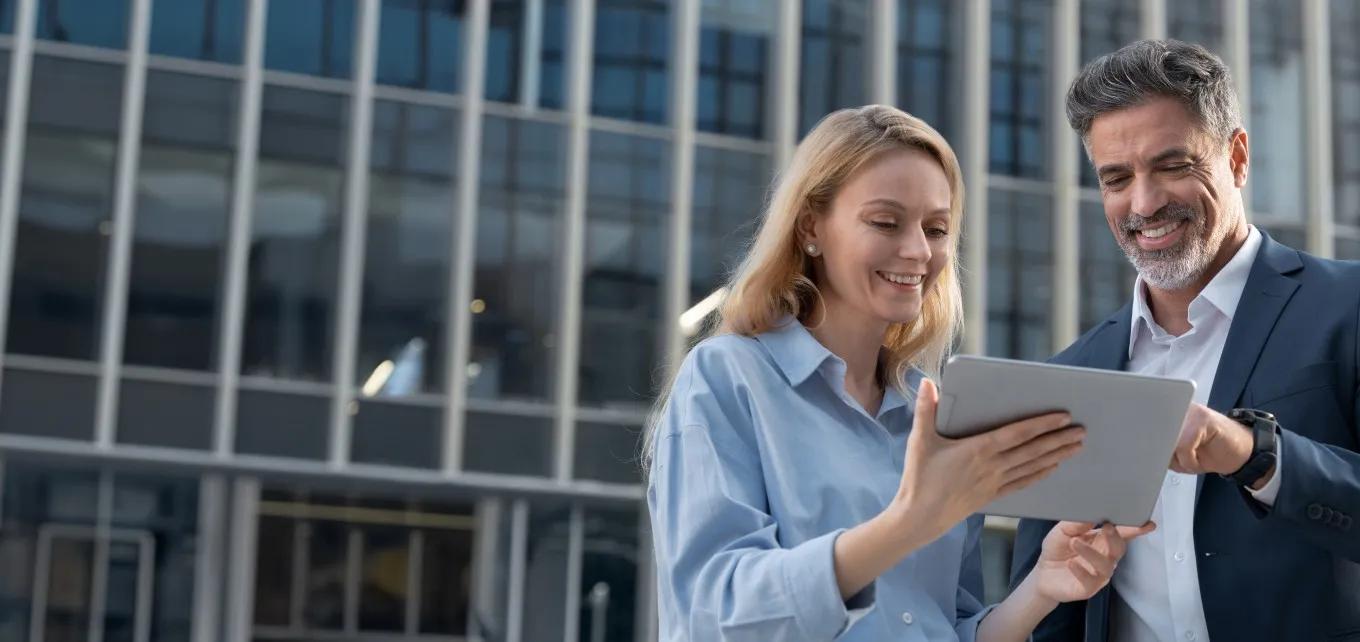business woman and man looking at at a laptop in from of an office building