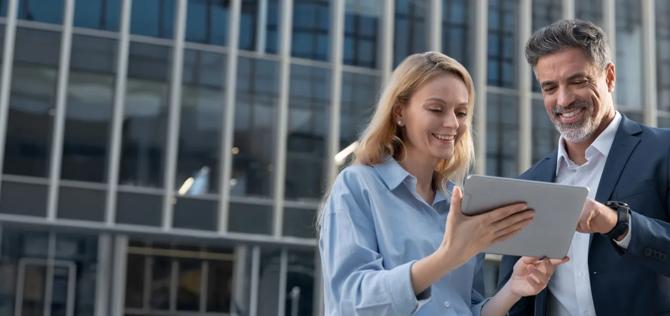 business woman and man looking at at a laptop in from of an office building