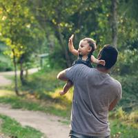 Father walking down a scenic outdoor lane holding his baby who is waving to a neighbor