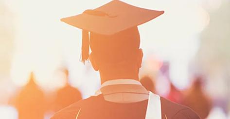 A young man walking away wearing a college cap and gown at graduation