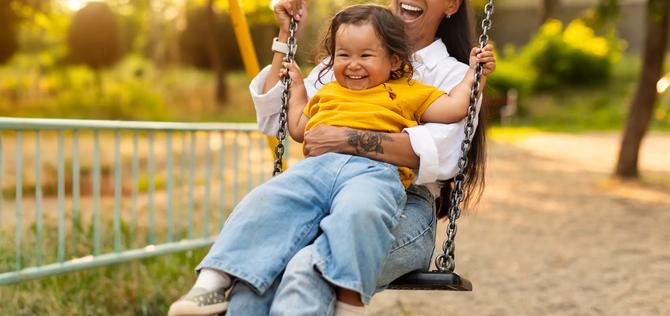 Playtime Moments. Japanese Mom Sitting With Her Toddler Infant Daughter, Swinging Baby And Having Fun on the Playground Outside, Sharing Laughter and Joyful Bonding In Park Outdoors