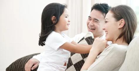 Happy Asian parents playing with their toddler daughter on a couch in the living room