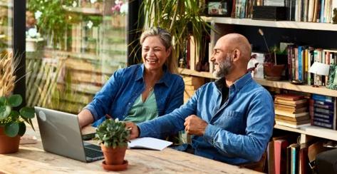 older married couple sitting at a table reviewing finances on a computer, looking pleased.