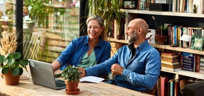 older married couple sitting at a table reviewing finances on a computer, looking pleased.