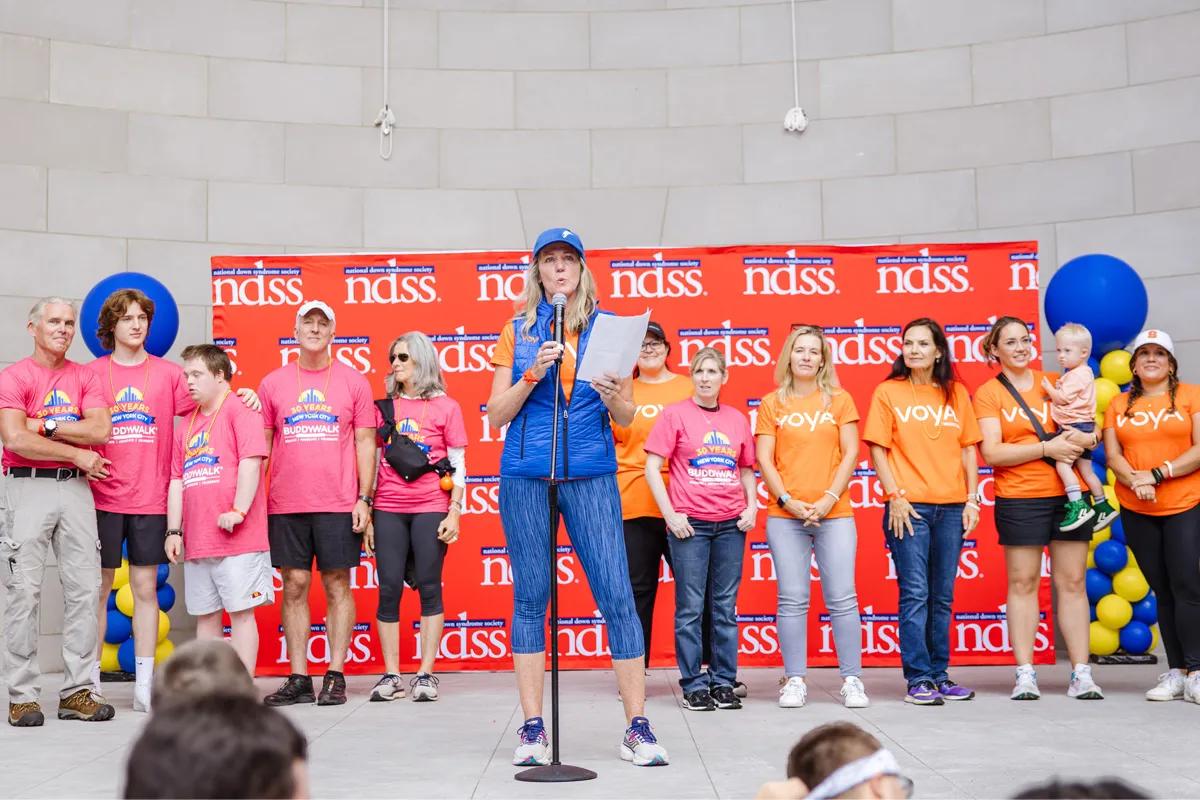 Woman speaking with large group of Voya employees wearing orange shirts supporting a walk through Central Park in New York City.