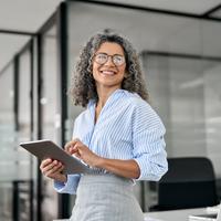 Smiling mature professional business woman bank manager, older happy female executive or lady entrepreneur holding digital tablet pad standing in office at work, looking away at copy space.