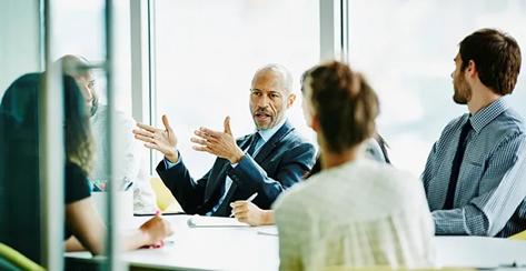 Coworkers are gathered around a modern office table, listening to their manager's pitch.