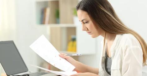 Pensive woman sitting down and analyzing a paper document.