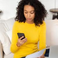 Young woman looking at her cellphone while on a laptop.