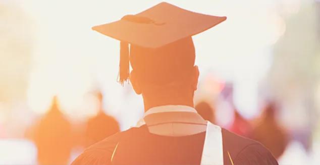 A young man walking away wearing a college cap and gown at graduation