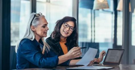 Two female colleagues laughing in conversation while discussing a business document