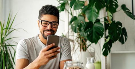 Young african american man eating breakfast and reading the news online. Handsome man using mobile phone