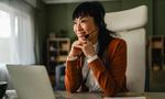Happy asian woman wearing a headset and smiling, sitting at her desk with a laptop, remotely working or communicating with clients from a home office environment