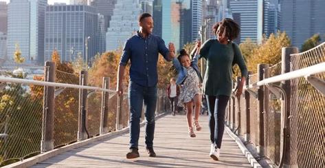 Black parents swinging their young daughter between them on a walking bridge in an urban setting