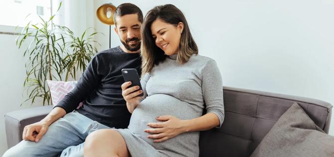 Adult couple expecting baby spending time together at home. Couple using smartphone.