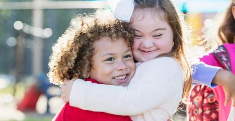 Girl with Down syndrome and her friend hugging each other and smiling