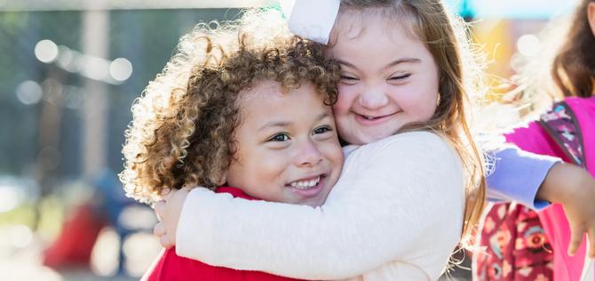 A pretty little girl with down syndrome and her cute 5 year old friend with curly hair, hugging each other and smiling.  The boy is mixed race African-American and Caucasian.