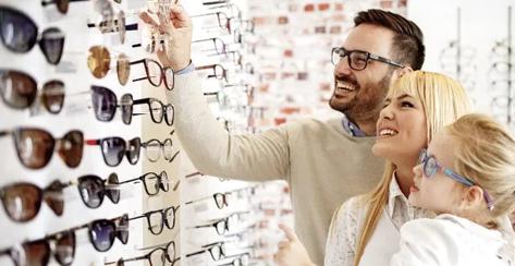 A couple with their young daughter browse glasses frame options at an optical shop.