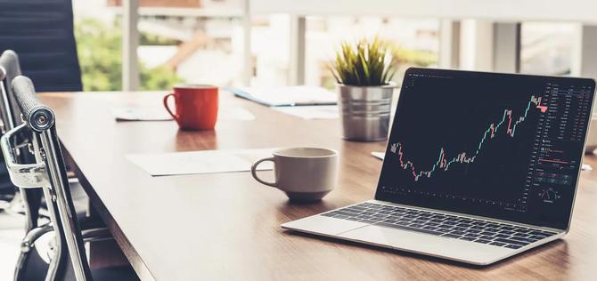 A computer on a table showing stocks going up and down on the screen.