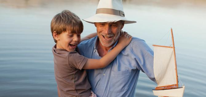 Smiling grandfather and grandson with toy sailboat wading in lake