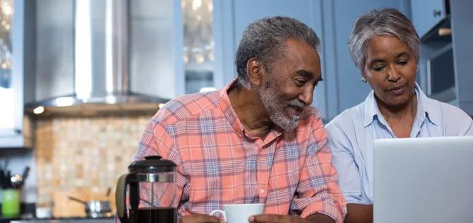 Senior couple in the kitchen drinking coffee while looking at a computer.