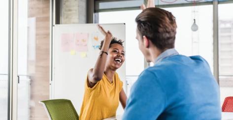 Two coworkers smiling and high fiving during a meeting