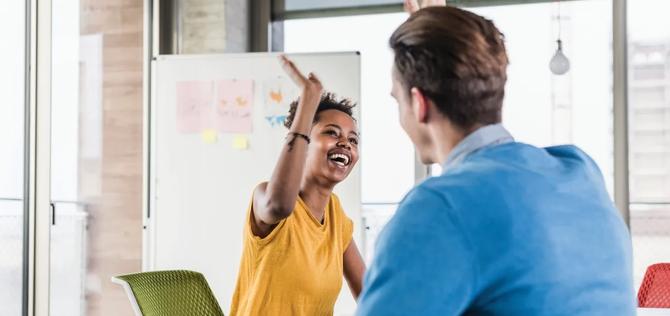 Two coworkers smiling and high fiving during a meeting