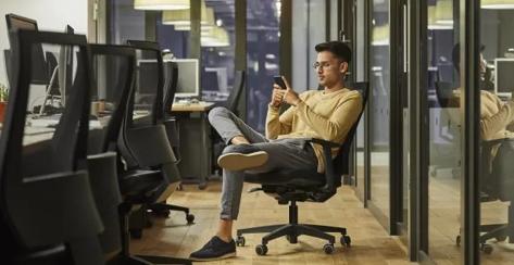 Young male employee sitting at his desk looking at his phone reviewing his benefits,