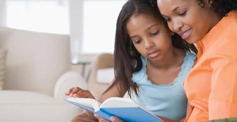 Side profile of a mid adult woman reading a book with her daughter and smiling