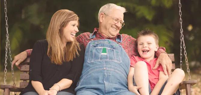 grandfather, daughter and grandson on a swing smiling