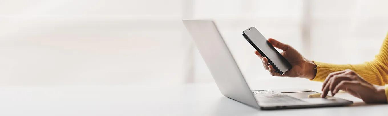 Person working with smartphone and laptop computer on table in office