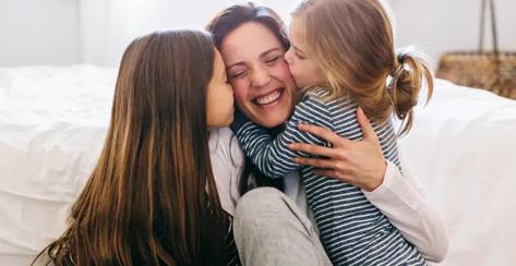 A mother with young daughters kissing either cheek.