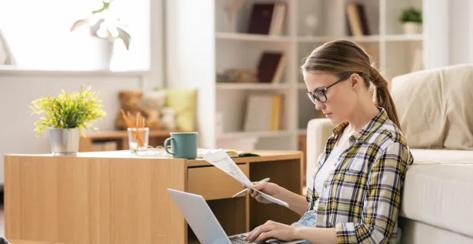 Young lady sitting on the floor in front of her couch looking over paperwork.