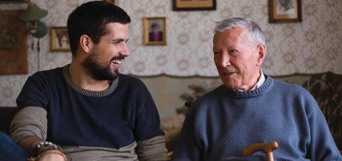 Younger man sitting with a mature man having a conversation and smiling 