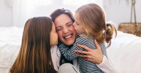 Mother with her two young daughters kissing either cheek.