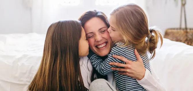 Mother with her two young daughters kissing either cheek.