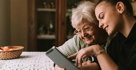 Smiling grandmother and granddaughter in the kitchen looking at a tablet.