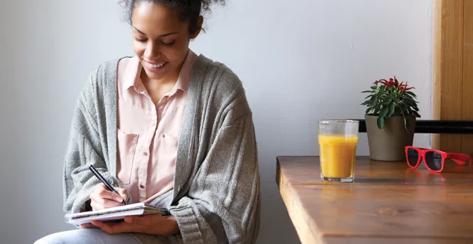 Young woman sitting at a table writing in a notebook.