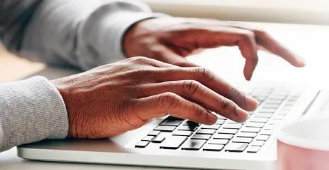 Hands typing on laptop with coffee mug off to the side.