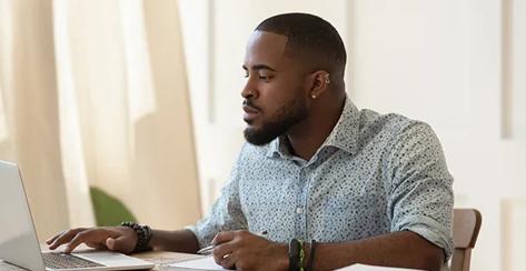 African man student sit at desk studying looking at laptop screen, guy holding pen noting in notepad useful info, online course activity, getting knowledge using internet websites, brain work concept
