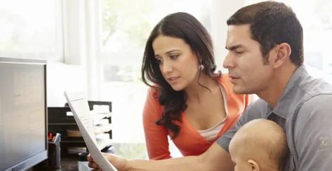 A young couple with their baby reviewing their finances in front of a computer. 