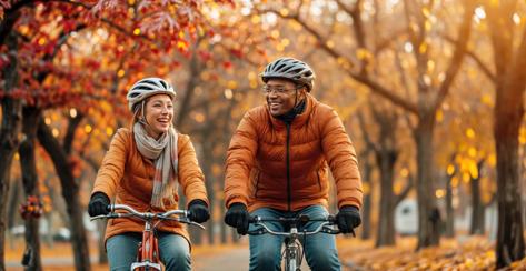 Senior couple on bikes. Happy people with bicycle in autumn park. Old people, man and woman with fall landscape background. Active cycle sport. Mature black couple exercises, healthy bike rides