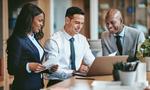 Smiling group of diverse businesspeople going over paperwork together and working on a laptop at a table in an office